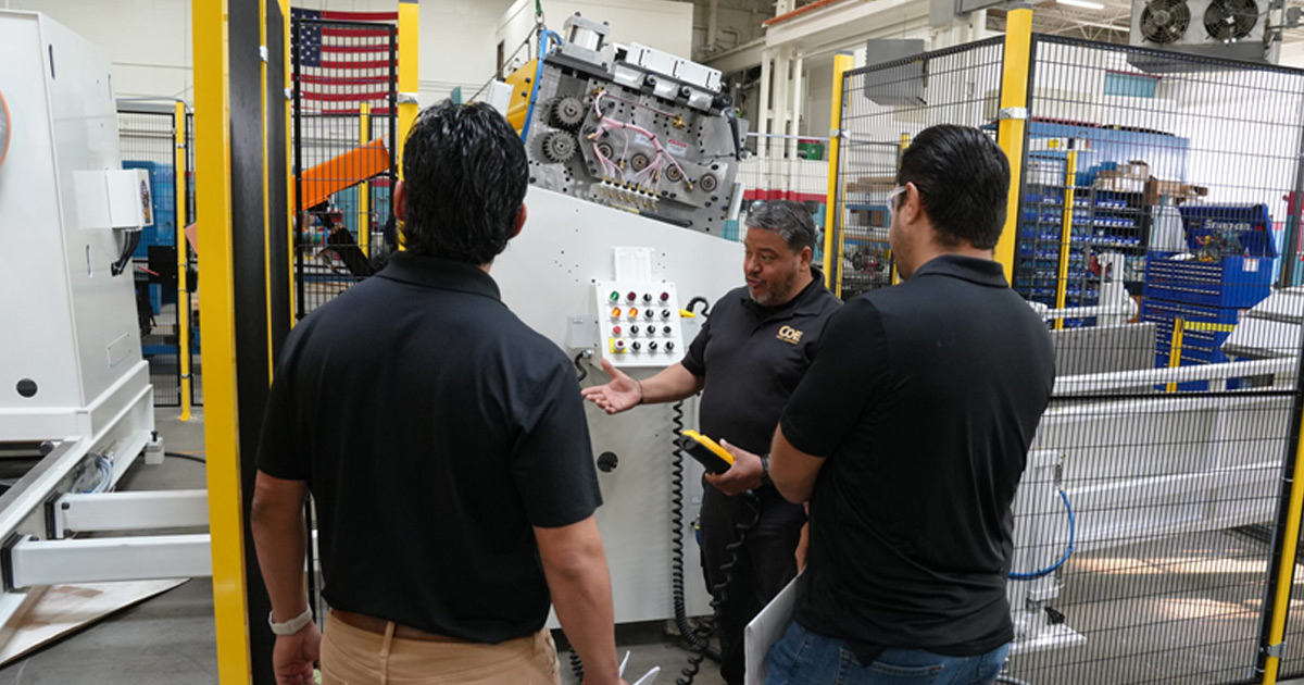 Customer tour in COE shop as a technician explains the machine control panel to two visitors.