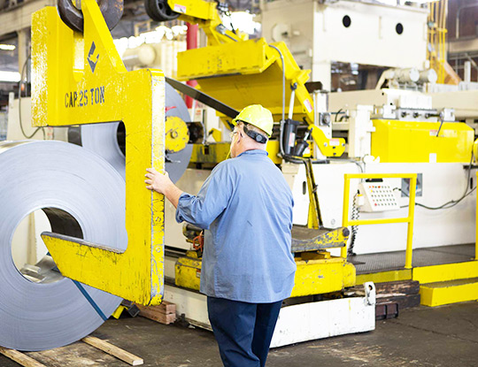 Overhead crane positioning a steel coil onto a coil car for staging and loading.
