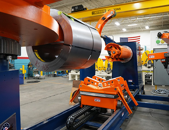 Turnstile-style coil handling system rotating a steel coil into position above a coil car for staging and loading.