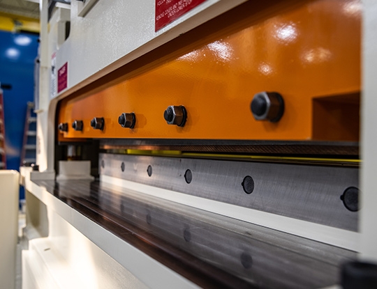 High strength steel stamping shear blade closeup showing the precision cutting edge and bolted blade assembly on a compact line.